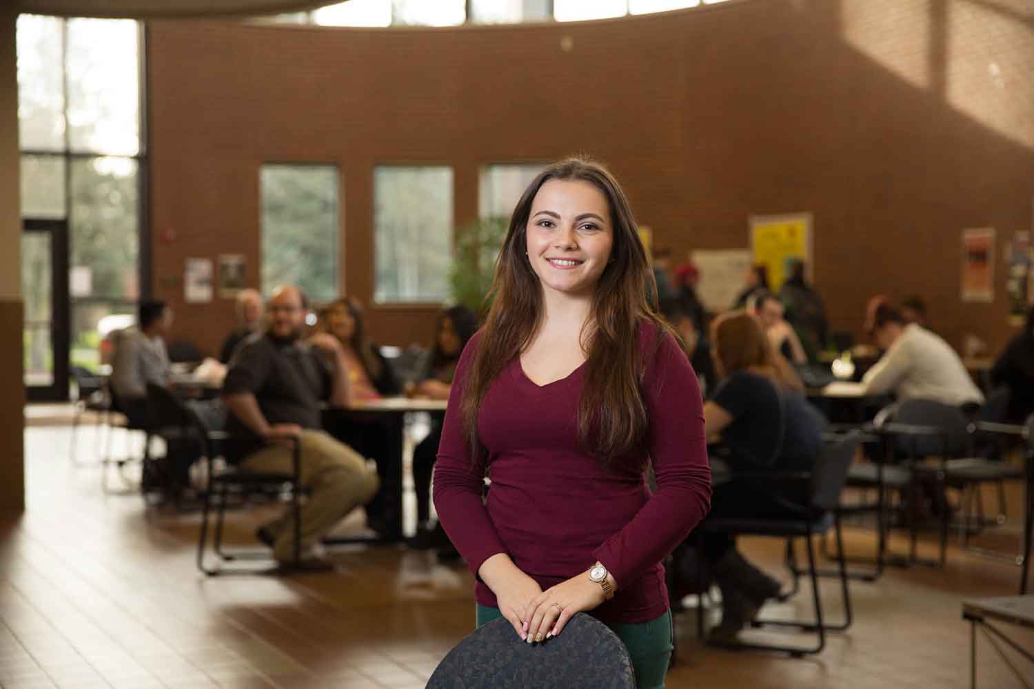 A student poses for the camera in front of a busy study area