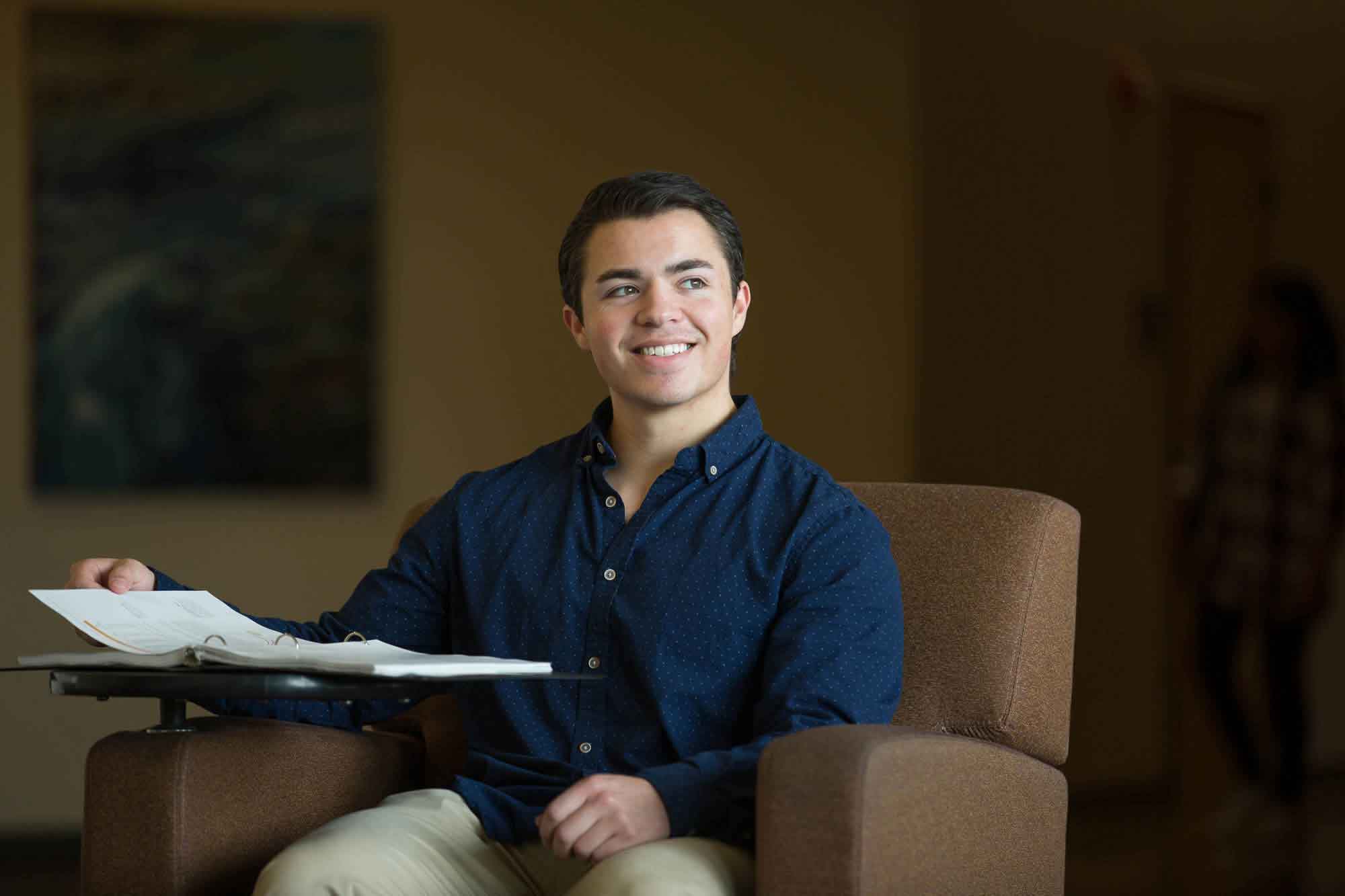 A student sitting in a hallway on campus leafs through his three-ring binder