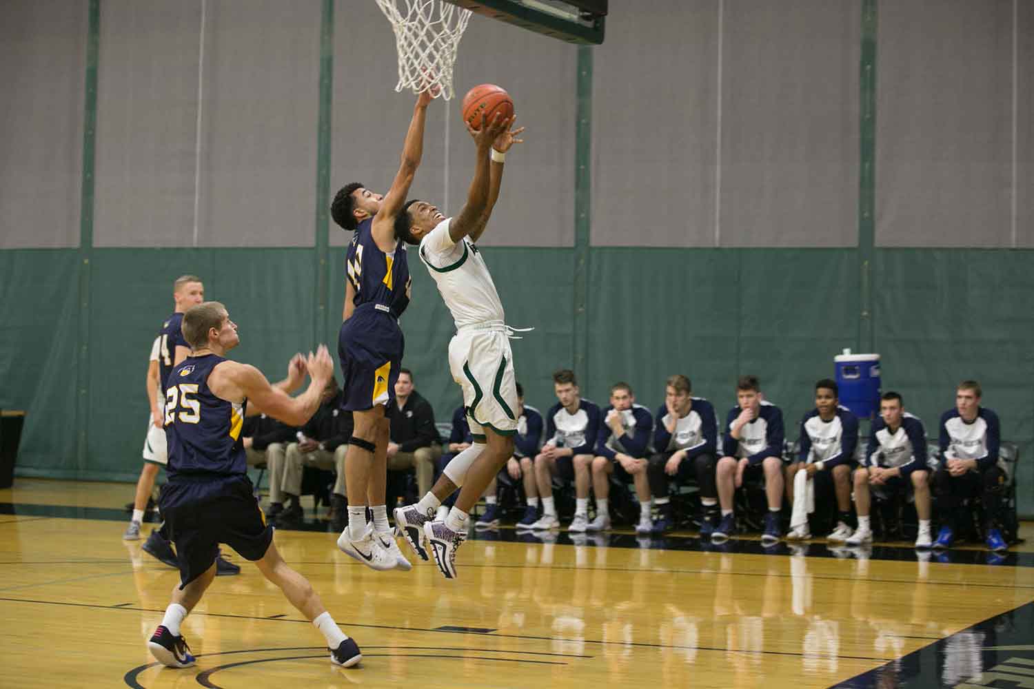 A men's basketball player tries for a basket while the opposing team tries to block