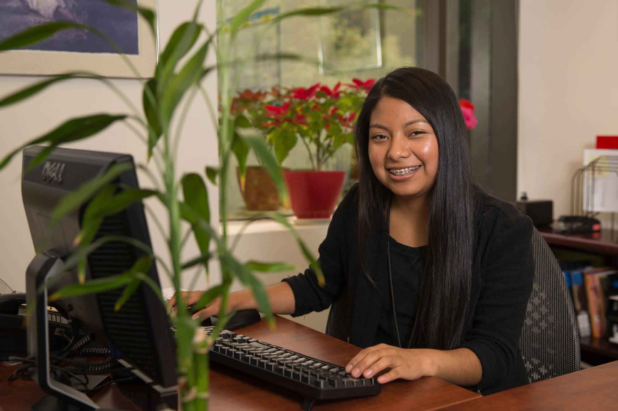 A woman works in an office with a pot of flowers in the background