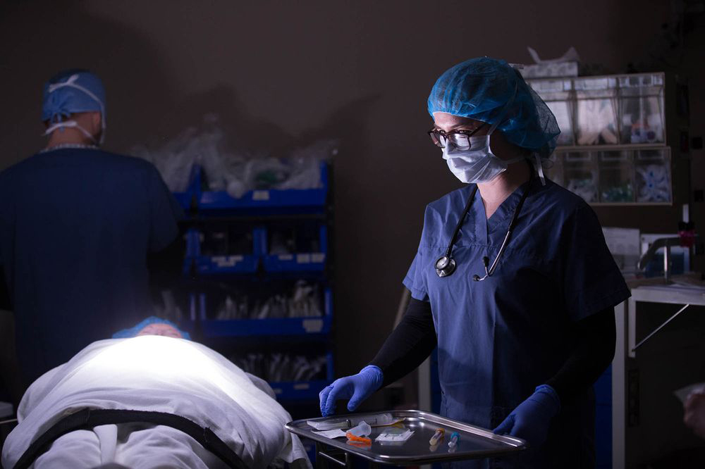 An anesthesia student in scrubs and mask working in a lab class